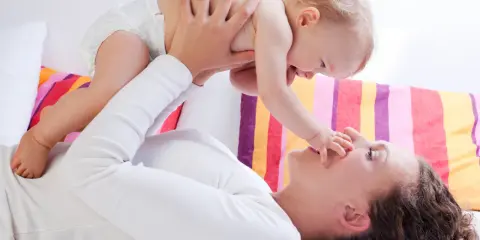 Mama podnosi dziecko, które wyciąga rączkę do jej nosa. Zdjęcie symbolizuje troskę o rozwój malucha, jak omega 3 dla niemowląt.