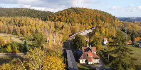 Jesienna panorama Gór Sowich. Widok na most kolejowy, tory i domy wśród kolorowych drzew. Atrakcje turystyczne regionu.