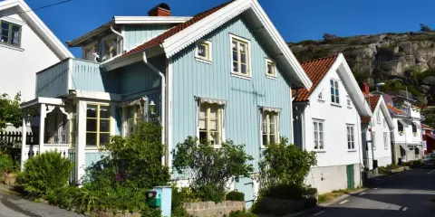 Blå och vita trähus längs en gata, med klippor i bakgrunden. Undrar hur mycket fastighetsskatt dessa vackra hus har.