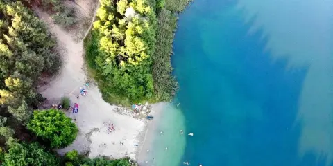 Plaża nad jeziorem tętni życiem. Ludzie odpoczywają na piasku, kąpią się w krystalicznie czystej wodzie, ciesząc się letnim dniem.