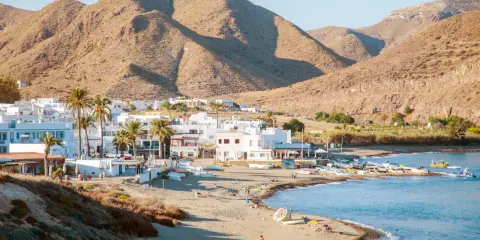 Pueblos de Almería con playa, casas blancas y palmeras junto a un mar azul, con montañas áridas de fondo.