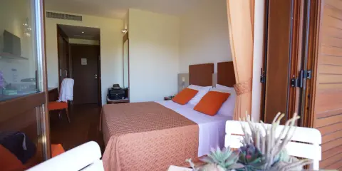 Camera accogliente al Valtur Otium Resort, con letto comodo, cuscini arancioni e vista sulla porta scorrevole in legno.