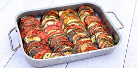 Un plat de tian de légumes, joliment arrangé en rondelles alternées de tomates, courgettes et aubergines, prêt à être dégusté.