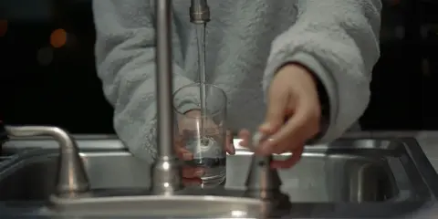 Mano llenando un vaso con agua del grifo, un problema común con el agua dura en España.