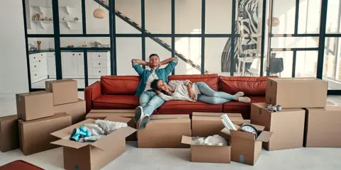 Couple se repose sur un canapé rouge entouré de cartons, signe d'un emménagement appartement réussi.