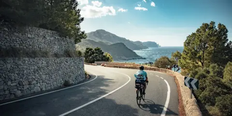 Rennradfahrer auf einer kurvigen Straße mit Blick auf das Meer und die Berge auf Mallorca.
