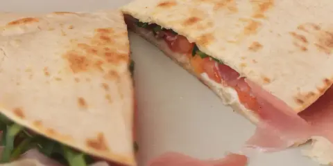 Pyszna piadina z szynką, pomidorami i rukolą, złożona na pół, prezentuje apetyczny przekrój.