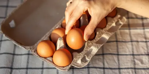 Dłoń wybiera jajko z wytłoczki. Zastanawiasz się, ile kcal ma jajko? To zdrowa przekąska!