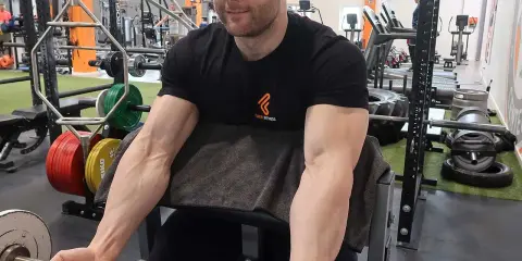 Mann trainiert Bizeps mit Langhantel im Fitnessstudio. Deutlich sichtbare Muskeln beim Bizeps dehnen.
