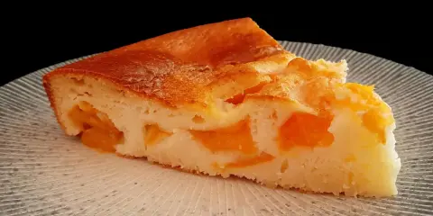 Tranche de clafoutis abricot, une création de chef, sur une assiette texturée.