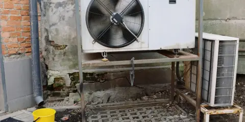 Unidad exterior de aire acondicionado goteando en invierno. Un cubo amarillo recoge el agua.