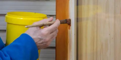 Persona aplica barniz a puerta de madera con brocha. Aprende como pintar puertas de madera para un acabado perfecto.