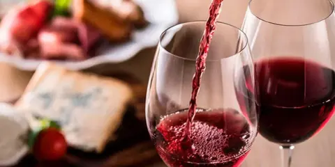 Vino tinto servido en copas, con tabla de quesos y embutidos al fondo. Una cata para apreciar la diferencia entre tempranillo y crianza.