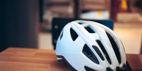Biały kask rowerowy na drewnianym stole. Pamiętaj o bezpieczeństwie, bo jazda bez kasku to mandat.