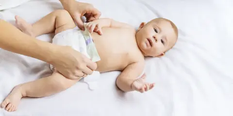 Rączki mamy zmieniają pieluszkę dziecku, by zapobiec odparzeniom. Maluch leży na białym tle.