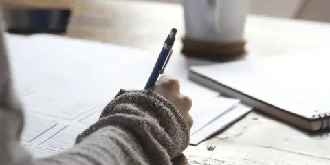 Ręka pisze na papierze, obok kubek kawy. Zastanawiam się, czy to formularze ZUS, czy może coś innego? ZFA co to jest?