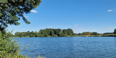 Blauer Himmel über dem ruhigen Linteler See, umgeben von üppigem Grün.