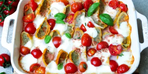 Herzhafter Maultaschen Auflauf mit Kirschtomaten und geschmolzenem Mozzarella, garniert mit frischem Basilikum.