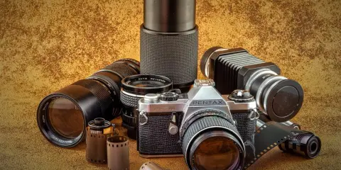 Kolekcja sprzętu fotograficznego: aparat Pentax JMC Super, obiektywy, mieszek i klisze.