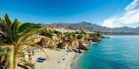 Sonnige playa de calahonda mit Palmen, weißem Sand, türkisfarbenem Meer und Bergen im Hintergrund.