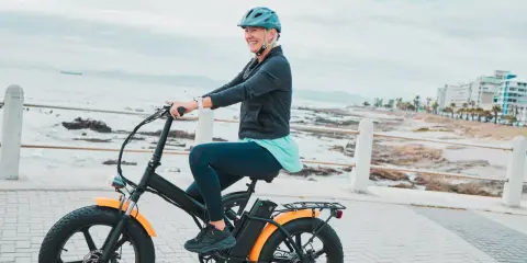 Une femme souriante roule sur un vélo électrique, profitant de la vue sur la mer. Le poid du vélo électrique ne l'empêche pas de profiter de sa balade.