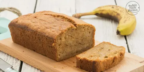 Saftiges Bananenbrot mit Skyr, frisch gebacken und auf einem Holzbrett angerichtet. Eine Banane liegt daneben.