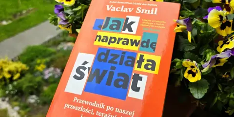 Książka Vaclava Smila "Jak naprawdę działa świat" wśród kwiatów. To przewodnik po przeszłości, teraźniejszości i przyszłości, który pomaga zrozumieć, co to odwyk od błędnych przekonań.