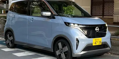 Nissan Sakura azzurro pastello, un'auto elettrica compatta con dettagli color rame sul tetto, parcheggiata su strisce pedonali.