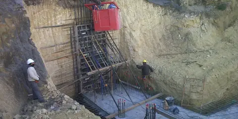 Trabajadores instalan encofrado para muro pantalla, con bataches y estructura de acero en obra.