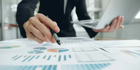 Un homme en costume analyse des graphiques et des diagrammes circulaires, tenant un stylo et un ordinateur portable. Il prépare un apport partiel d'actif.
