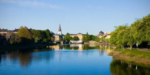 Vacker vy över Klarälven i Karlstad med stadens silhuett och grönska. Perfekt för promenader och andra aktiviteter Karlstad erbjuder.