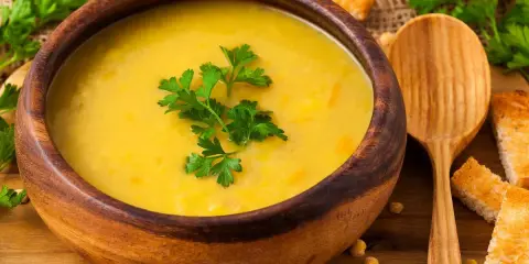 Vellutata di ceci cremosa in ciotola di legno, guarnita con prezzemolo fresco e accompagnata da crostini dorati.