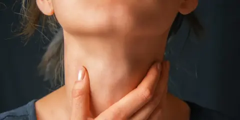 Zbliżenie na szyję osoby trzymającej się za gardło.