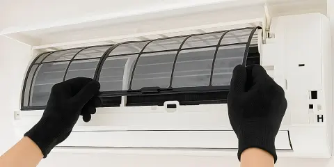 Mani con guanti neri estraggono i filtri da un condizionatore, mostrando come pulire i filtri del condizionatore per un'aria più fresca.