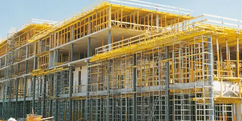 Edificio en construcción con intrincadas estructuras temporales amarillas y grises, sosteniendo los pisos de concreto.