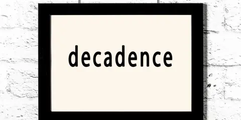 Czarny prostokątny obraz z napisem "decadence" na jasnym tle, wiszący na białej ceglanej ścianie. Symbol dekadentyzmu.
