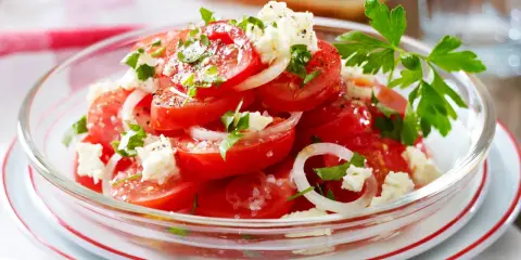 Frischer Tomatensalat mit Feta, Zwiebeln und Petersilie, garniert mit grobem Salz und Pfeffer. Ein leichter Genuss!