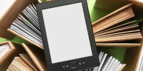 Un e-reader con schermo bianco è circondato da libri aperti, pronti per essere letti.