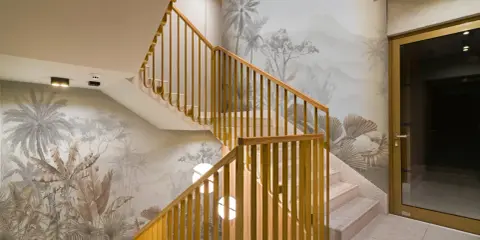 Habillage mur cage d'escalier avec un décor tropical en camaïeu. Escalier en marbre et rambarde en bois doré.