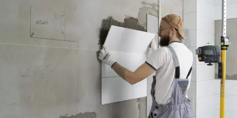 Obrero coloca baldosas en pared, usando nivel láser para asegurar un acabado perfecto. El proceso de instalación de aislante paredes interiores avanza.