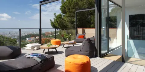 Cómodo balcón terraza con sillones, pufs naranjas y mesas bajas, con vistas a la ciudad.