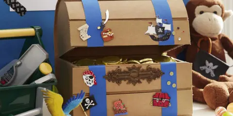 Bastelidee: Eine Schatztruhe aus Pappe, verziert mit Piratenmotiven und gefüllt mit Goldmünzen. Ein Affe hält eine Piratenflagge.