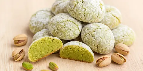 Amaretti pistache saupoudrés de sucre glace, avec des pistaches entières et décortiquées. Une recette gourmande à découvrir.