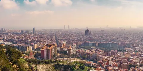 Panorama von Barcelona von oben. Die Sagrada Familia und moderne Wolkenkratzer ragen aus der weitläufigen Stadt hervor.