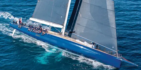Un grand voilier bleu glisse sur l'eau, tel un tapis volant bateau. L'équipage est à bord, profitant de la navigation.