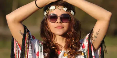 Dziewczyna w stylu boho, z wiankiem z kwiatów i okularami, w kwiecistej bluzce. Jej moda nawiązuje do wolności i natury, jak u dzieci kwiatów.