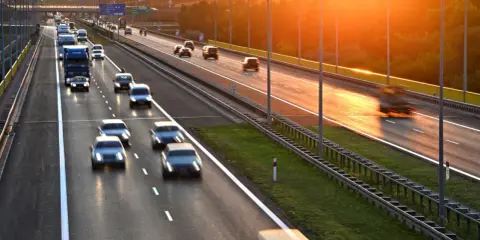 Zachód słońca nad Via Baltica. Samochody i ciężarówki pędzą autostradą w złotym blasku.