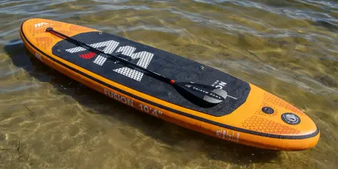 Pomarańczowy aquamarina sup z wiosłem leży na płytkiej, przejrzystej wodzie.
