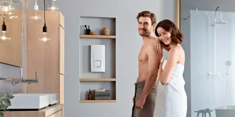 Glückliches Paar im Bad, neben dem besten Durchlauferhitzer. Modernes Bad mit Dusche und Waschbecken.