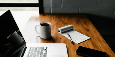 Laptop, kawa, notatnik i telefon na drewnianym biurku. Czas pomyśleć, jak zakonczyc bloga po ang.